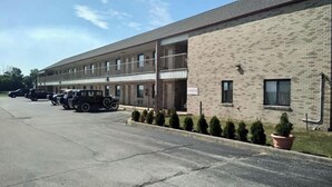 A motel with a brick facade, multiple balconies, and a parking lot with several vehicles. - Hoosier Inn (Portland)