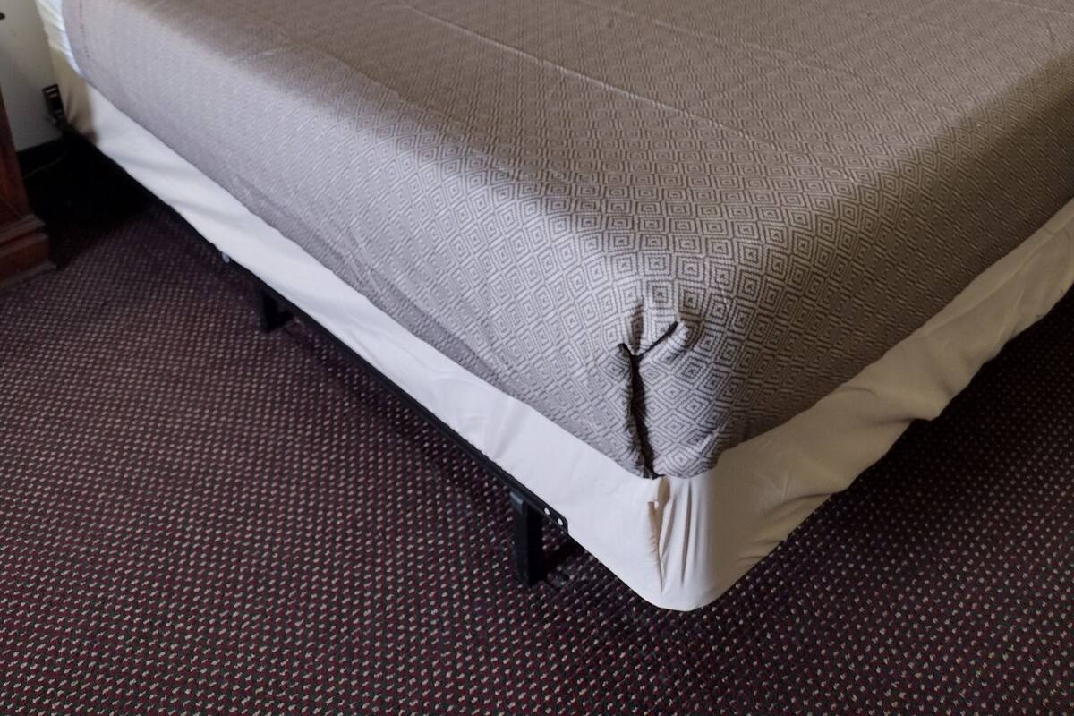 A neatly made bed with a patterned bedspread, a wooden headboard, and a single bedside lamp.