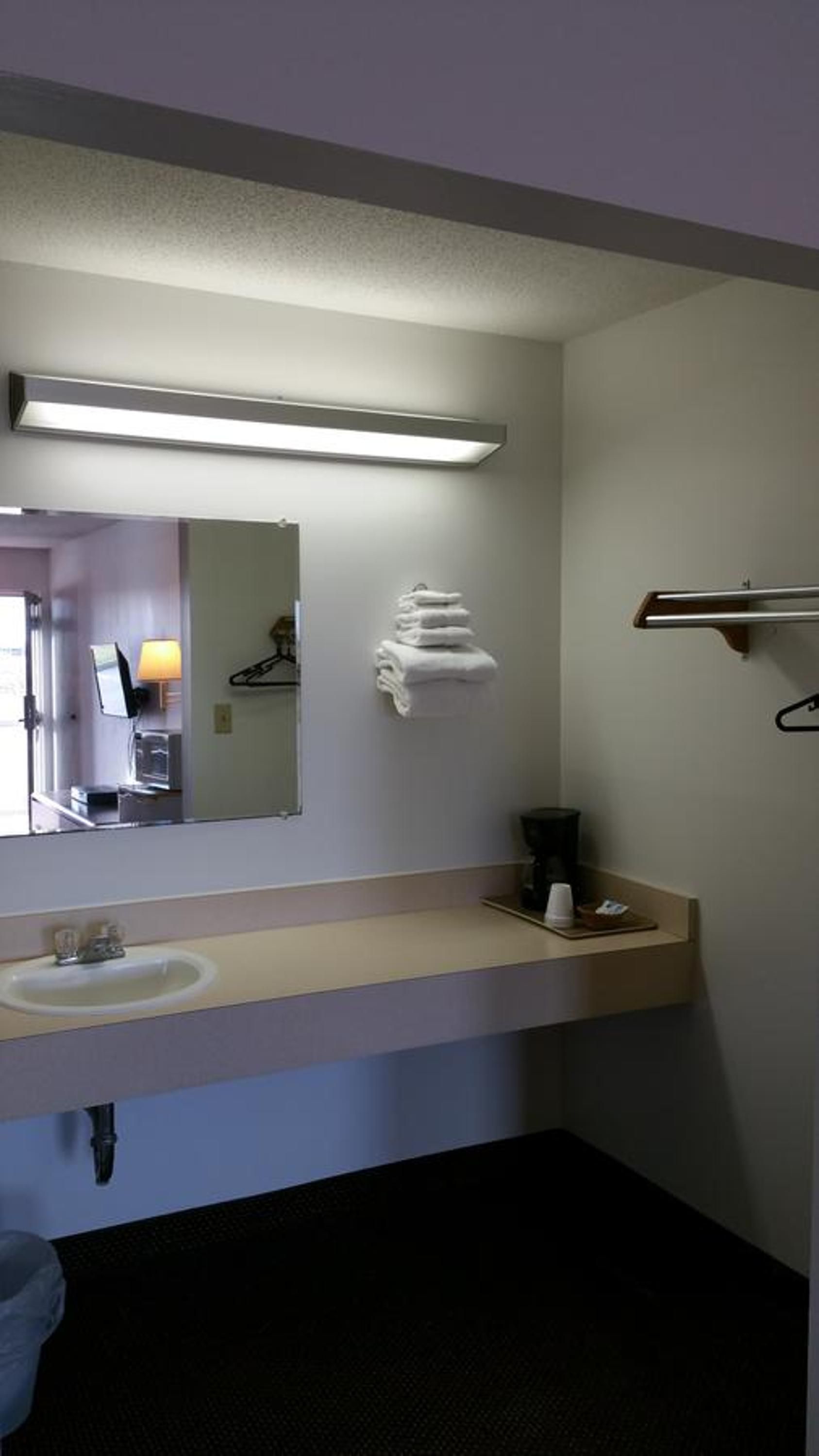 A hotel bathroom with a sink, mirror, towel rack, and a towel stack.