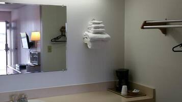 A hotel bathroom with a sink, mirror, towel rack, and a towel stack.
