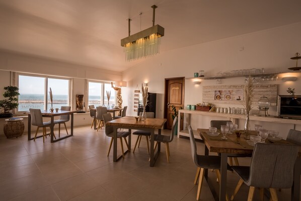 A spacious dining area with a view of the sea, a wooden table, and modern chairs. - Sandhi House - Yoga & Wellness (Mafra)