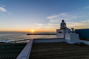 Una estatua de Buda en una azotea con vista al atardecer sobre el océano.