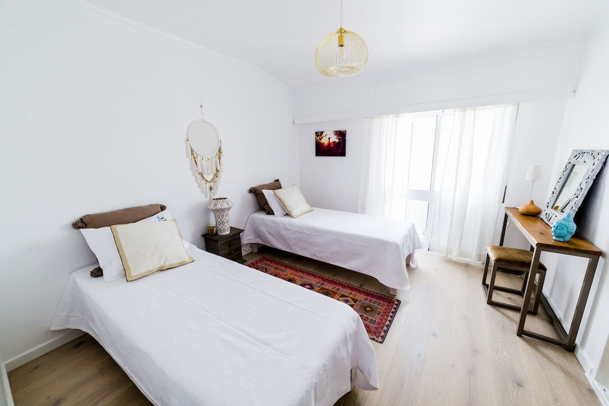 Ein Zimmer mit zwei Betten, Holzboden, einer Pendelleuchte, einem kleinen Tisch und einem Stuhl.