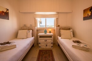 Un dormitorio con dos camas, una mesita de noche con lámpara y una ventana con vistas.