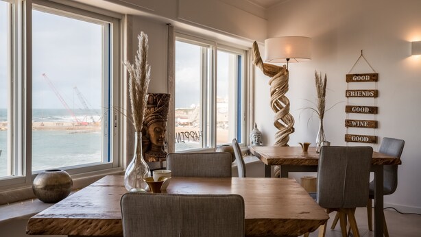 Een eetgedeelte met uitzicht op zee, een houten tafel, stoelen en een wand met decoratieve borden.