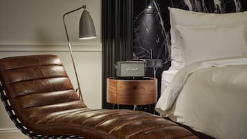 A leather armchair with metal frame, a bedside table with a vintage radio, and a bed with white linens.