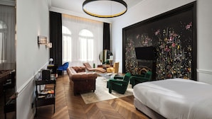Una habitación de hotel moderna con una cama grande, una zona de estar con sofá y sillones, un televisor y una obra de arte floral de gran tamaño en la pared.