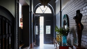 Un pasillo con una puerta negra, una ventana con marco verde y una estatua.