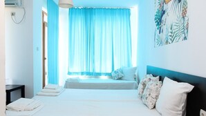 A hotel room with a bed, a window with blue curtains, a bedside table, and a wall with a tropical-themed artwork. - Salena Beach Hotel (Primorsko)
