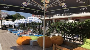 A poolside area with lounge chairs and bean bags, umbrellas, and a wooden bench. - Salena Beach Hotel (Primorsko)
