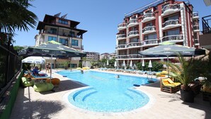 A swimming pool area with lounge chairs and umbrellas, surrounded by buildings with balconies. - Salena Beach Hotel (Primorsko)