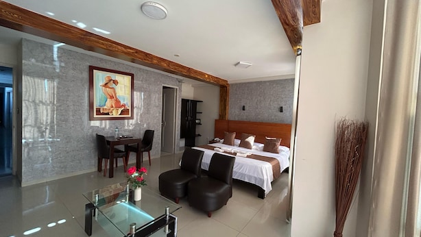 A modern hotel room with a large bed, a dining area with a glass table, and a painting on the wall. - Aura Hotel (Chiclayo)