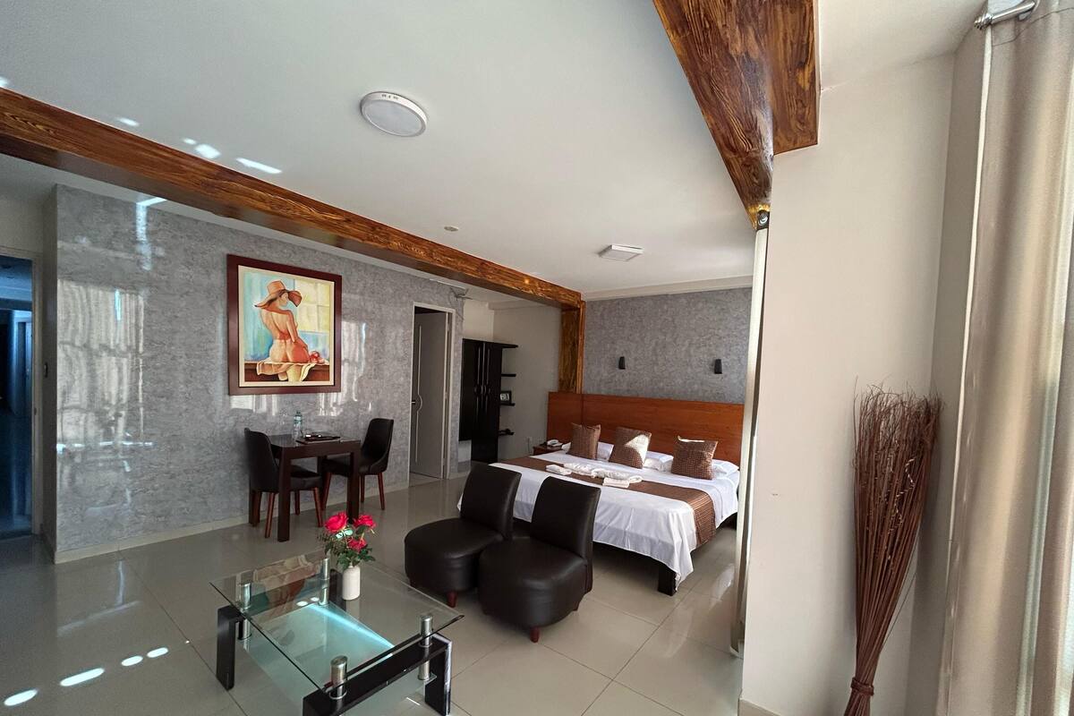 Une chambre d’hôtel moderne avec un grand lit, un coin repas doté d’une table en verre et un tableau au mur.