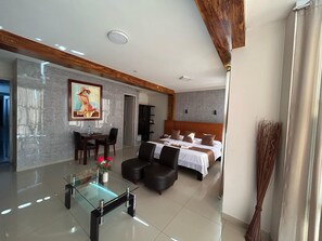 A modern hotel room with a large bed, a dining area with a glass table, and a painting on the wall. - Aura Hotel (Chiclayo)