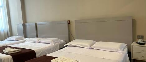 A hotel room with two beds, each with white linens and brown headboards. There are bedside tables with lamps and a phone.