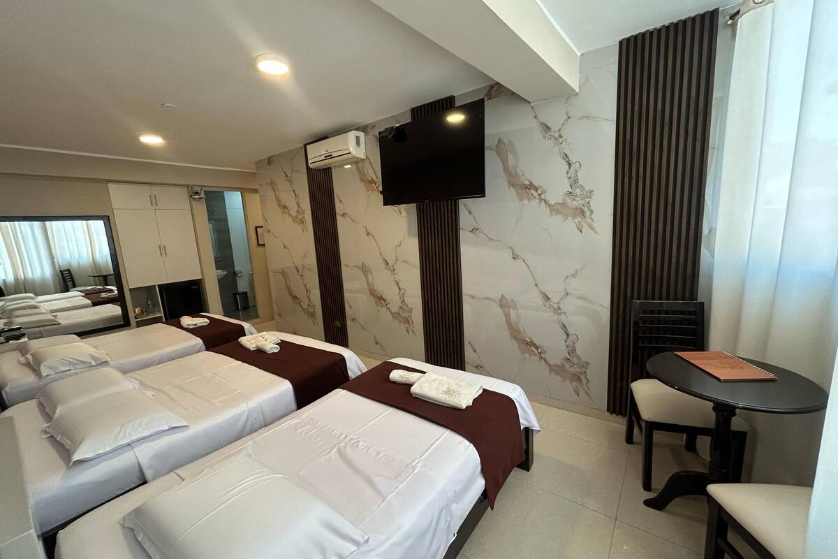 Une chambre d’hôtel avec trois lits, un téléviseur fixé au mur, une petite table et une chaise.