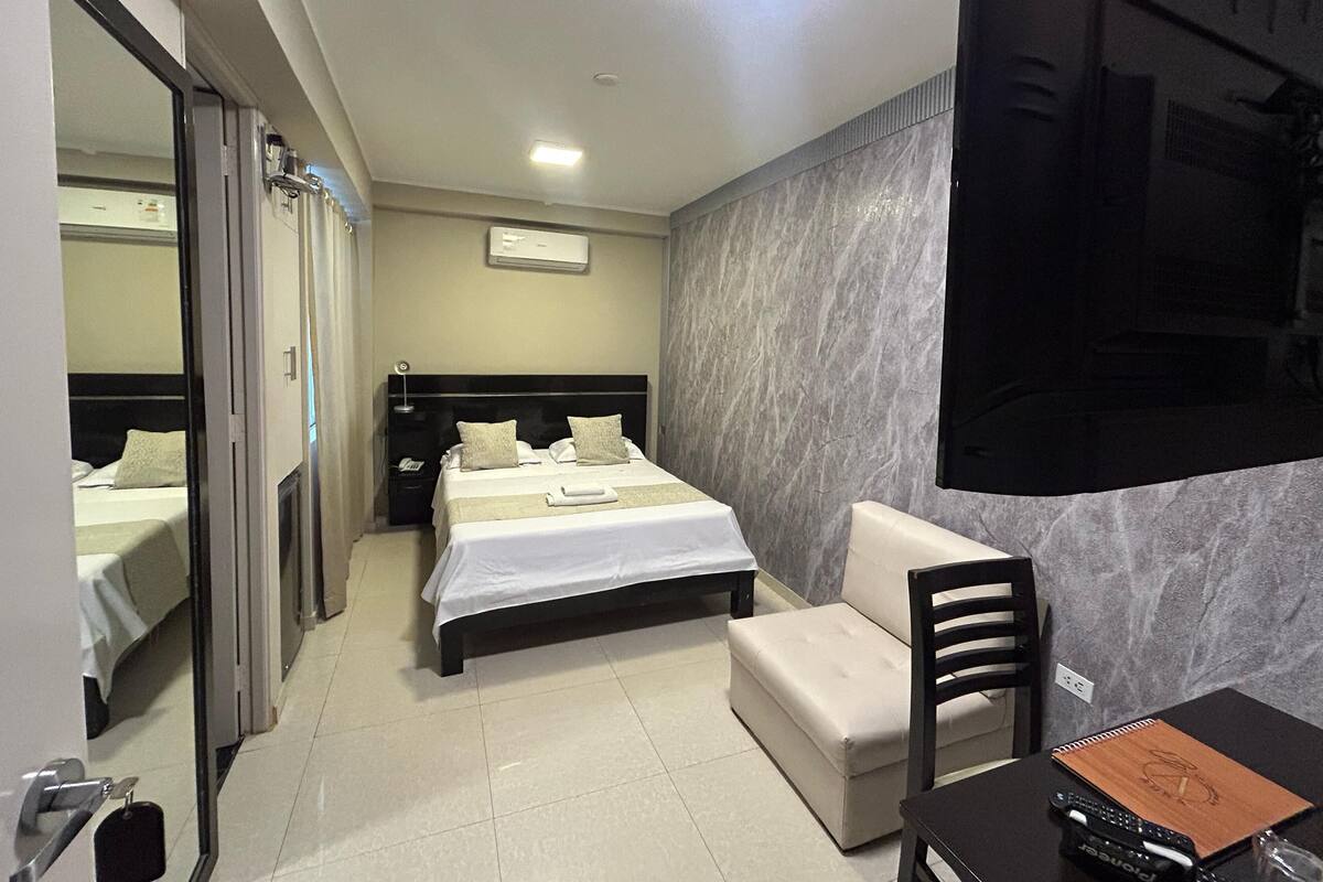 Une chambre d’hôtel avec un lit, un bureau, une chaise et un grand miroir.