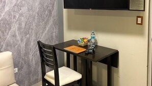 A small, private room with a flat-screen TV mounted on the wall, a small table with a notebook, a bottle of water, and a basket of snacks. - Aura Hotel (Chiclayo)