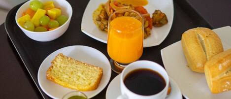 A tray with breakfast items including toast, fruit, a glass of orange juice, a cup of coffee, and bread rolls.