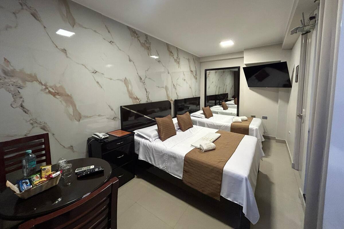 Une chambre d’hôtel avec deux lits, un bureau avec une chaise, une télévision et un mur décoré d’un motif imitant le marbre.