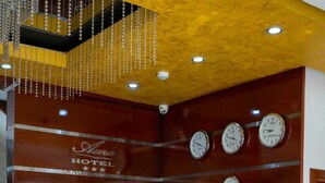 A hotel reception desk with a wooden finish, multiple clocks, and a security camera. - Aura Hotel (Chiclayo)
