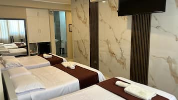 Ein Hotelzimmer mit drei Betten, einem Fernseher, einer Klimaanlage und einem durchgegangenen Badezimmer.