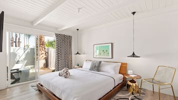 A modern bedroom with a large bed, a chair, a small table, and a view of the outdoors.