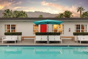 A poolside area with white lounge chairs, a red door, and a teal umbrella. - the Weekend (Palm Springs)
