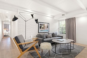 A modern living room with a grey sofa, a wooden chair, a round coffee table, and a floor lamp. - The Weekend by AvantStay (Palm Springs)