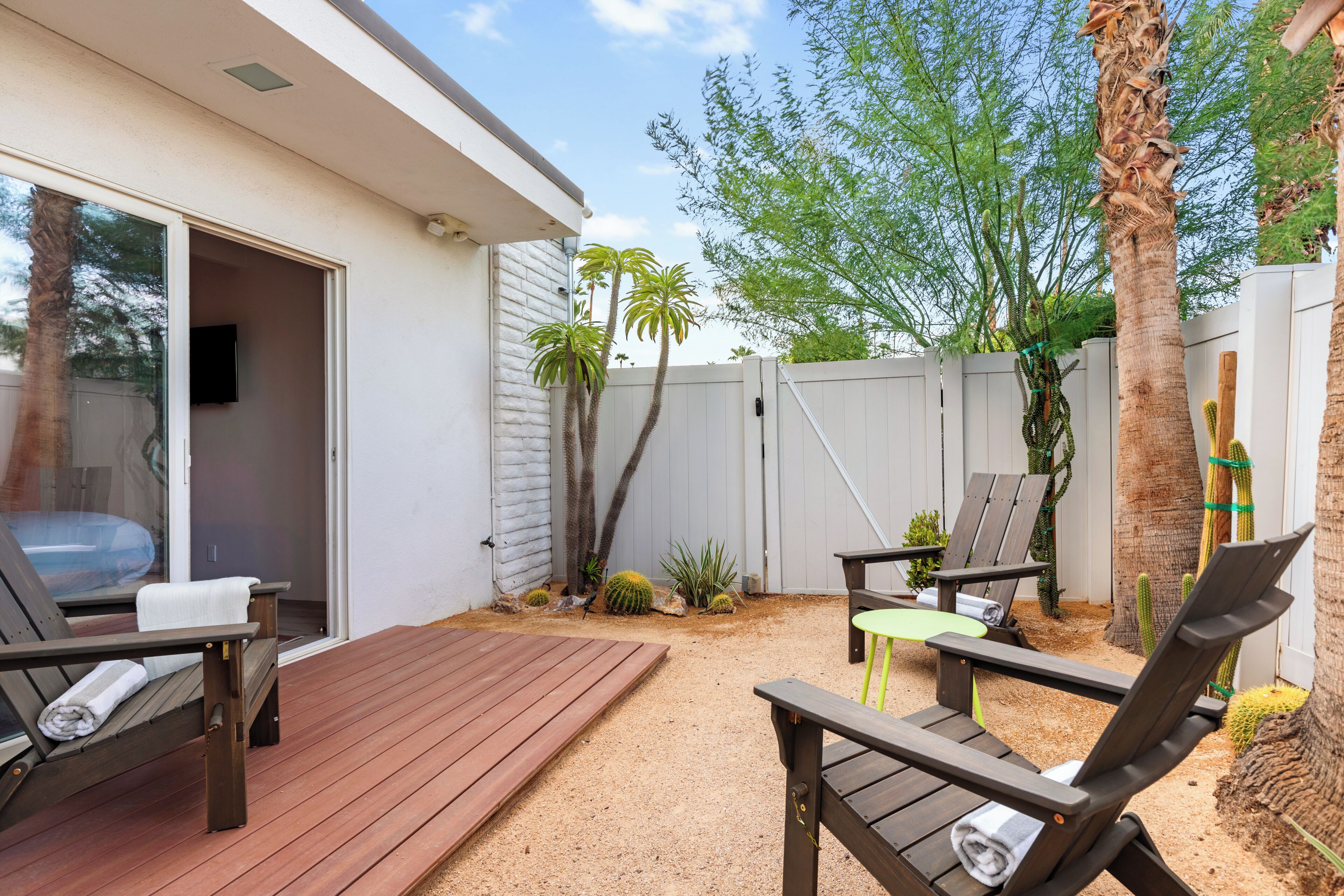 Une terrasse dotée de meubles en bois, d’une clôture blanche et de quelques cactus.