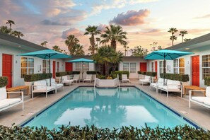 A pool area with white lounge chairs and blue umbrellas, surrounded by palm trees and a sunset sky. - the Weekend (Palm Springs)