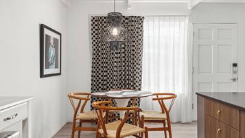 Un coin repas avec une table ronde, quatre chaises en bois, un rideau à motifs, un luminaire suspendu et une porte blanche.