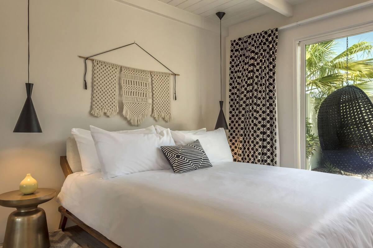 A bed with white linens, a black and white patterned pillow, and macrame wall hangings.