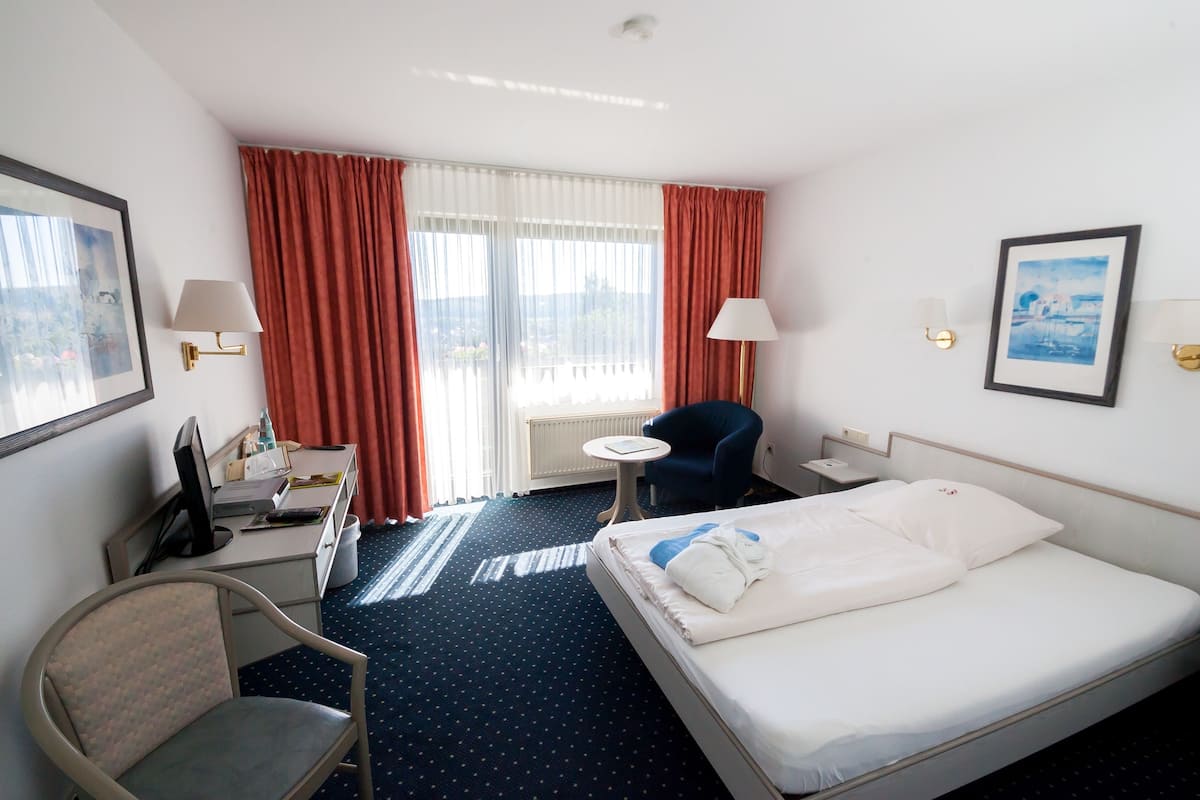 Une chambre d’hôtel avec un lit, un bureau, une chaise et une fenêtre avec des rideaux.