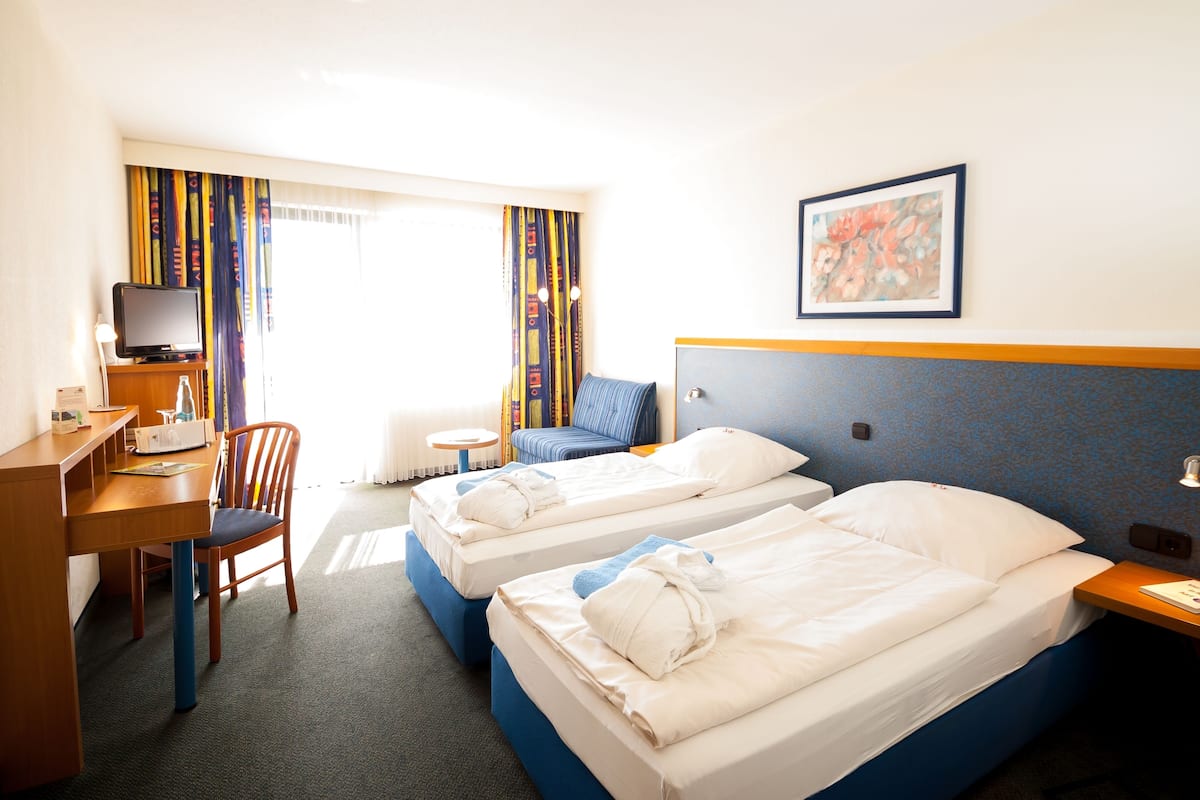 Une chambre d’hôtel avec deux lits, un bureau avec un ordinateur, une chaise et une fenêtre avec des rideaux.