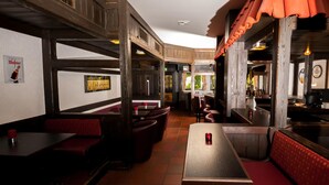 Een restaurant met zitbanken en tafels, houten balken en een betegelde vloer.