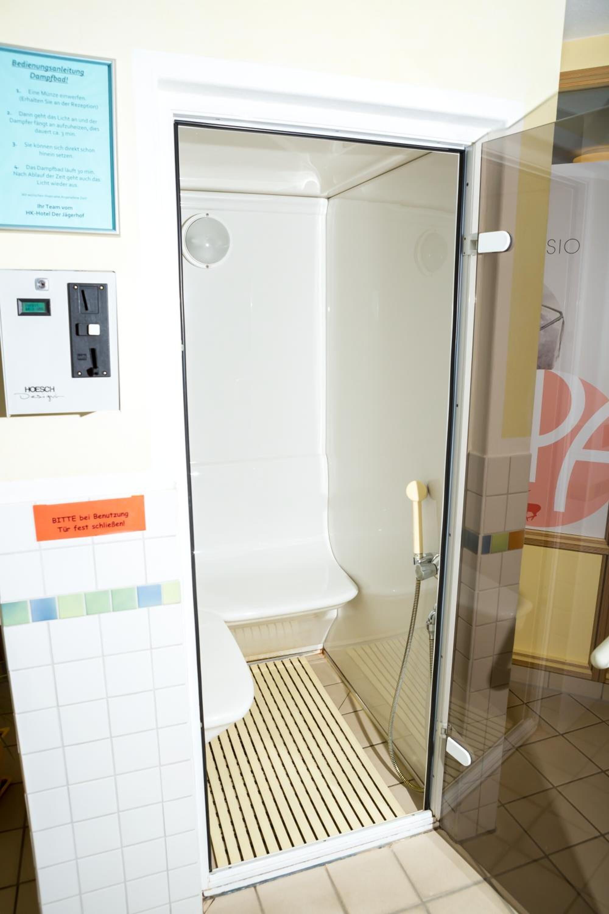 A glass-enclosed shower area with a control panel and a sign indicating usage instructions.
