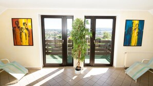 Een kamer met een groot raam, een plant in pot en twee fauteuils.