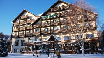 A multi-story hotel with a prominent "HOTEL" sign, balconies, and a snow-covered playground area.