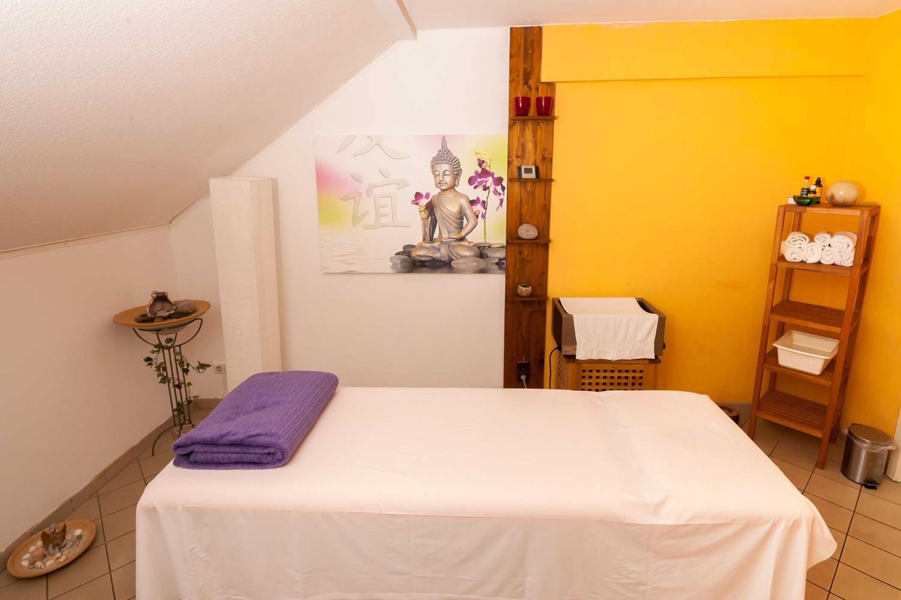 Un dormitorio con cama, un cuadro, estante con toallas y una mesita con planta.