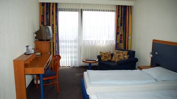A hotel room with a bed, a desk with a television, a chair, and a sofa.