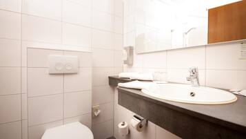 Un bagno moderno con il water bianco, un lavandino con piano d'appoggio scuro e uno specchio sopra il lavandino.