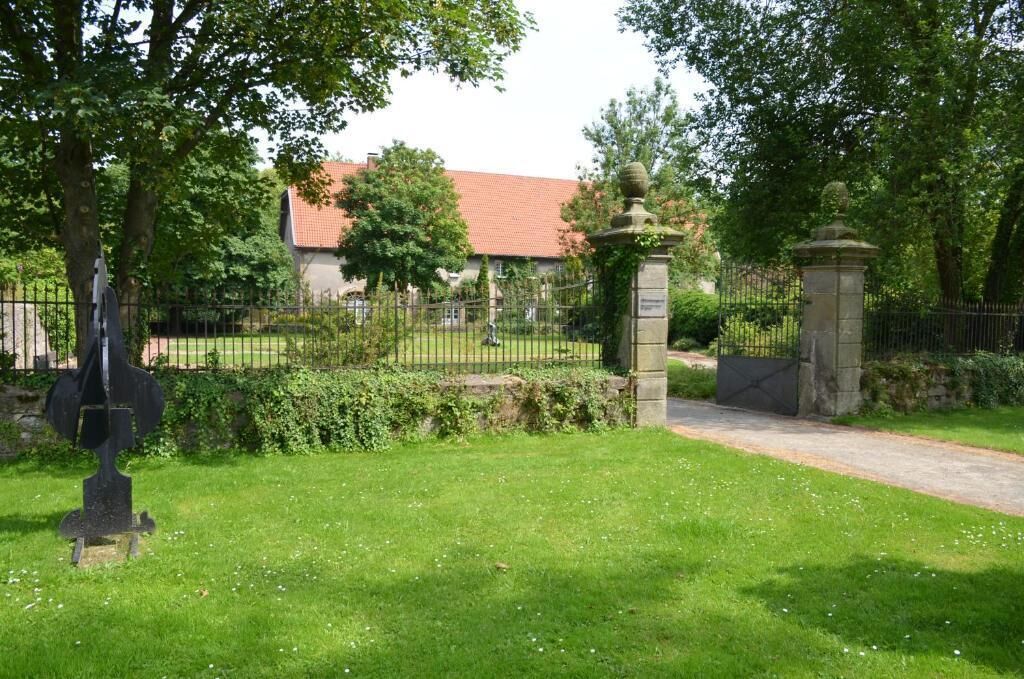 A gated entrance to a building with a red-tiled roof, surrounded by a well-maintained lawn and a metal fence.