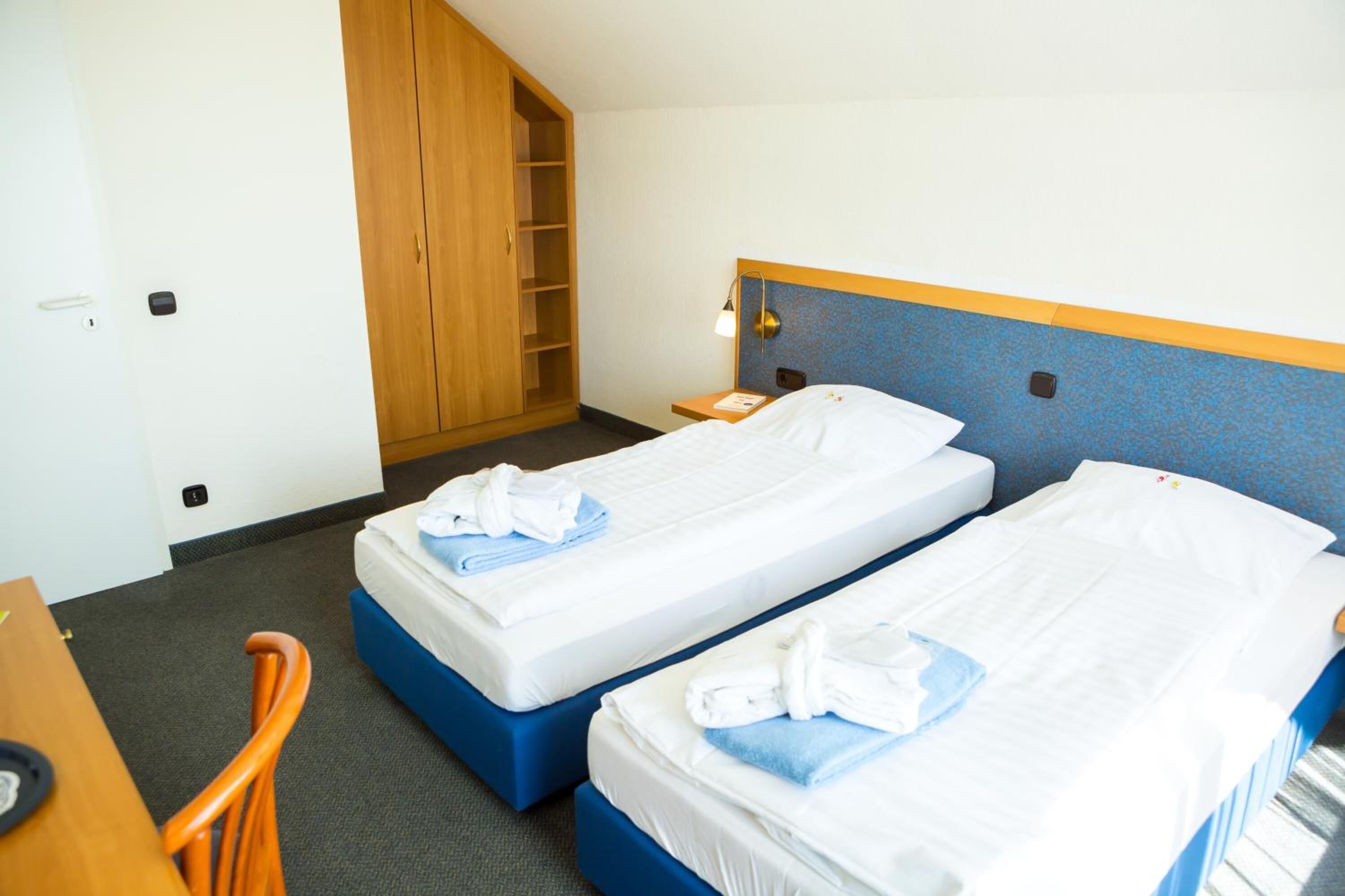 A hotel room with two beds, a desk, a chair, and a wardrobe.