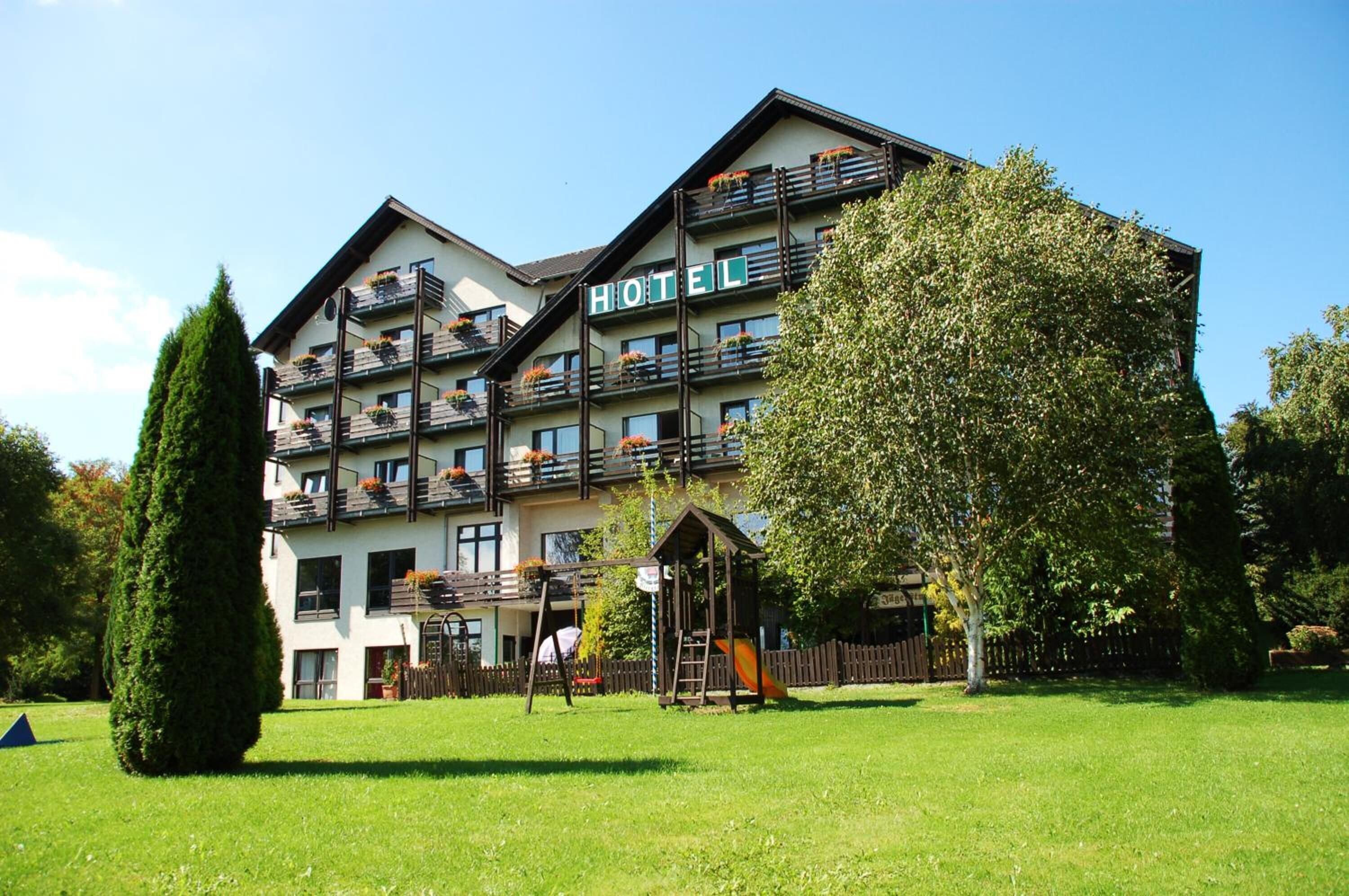 Et hotel med flere balkoner, en legeplads og en velholdt græsplæne.