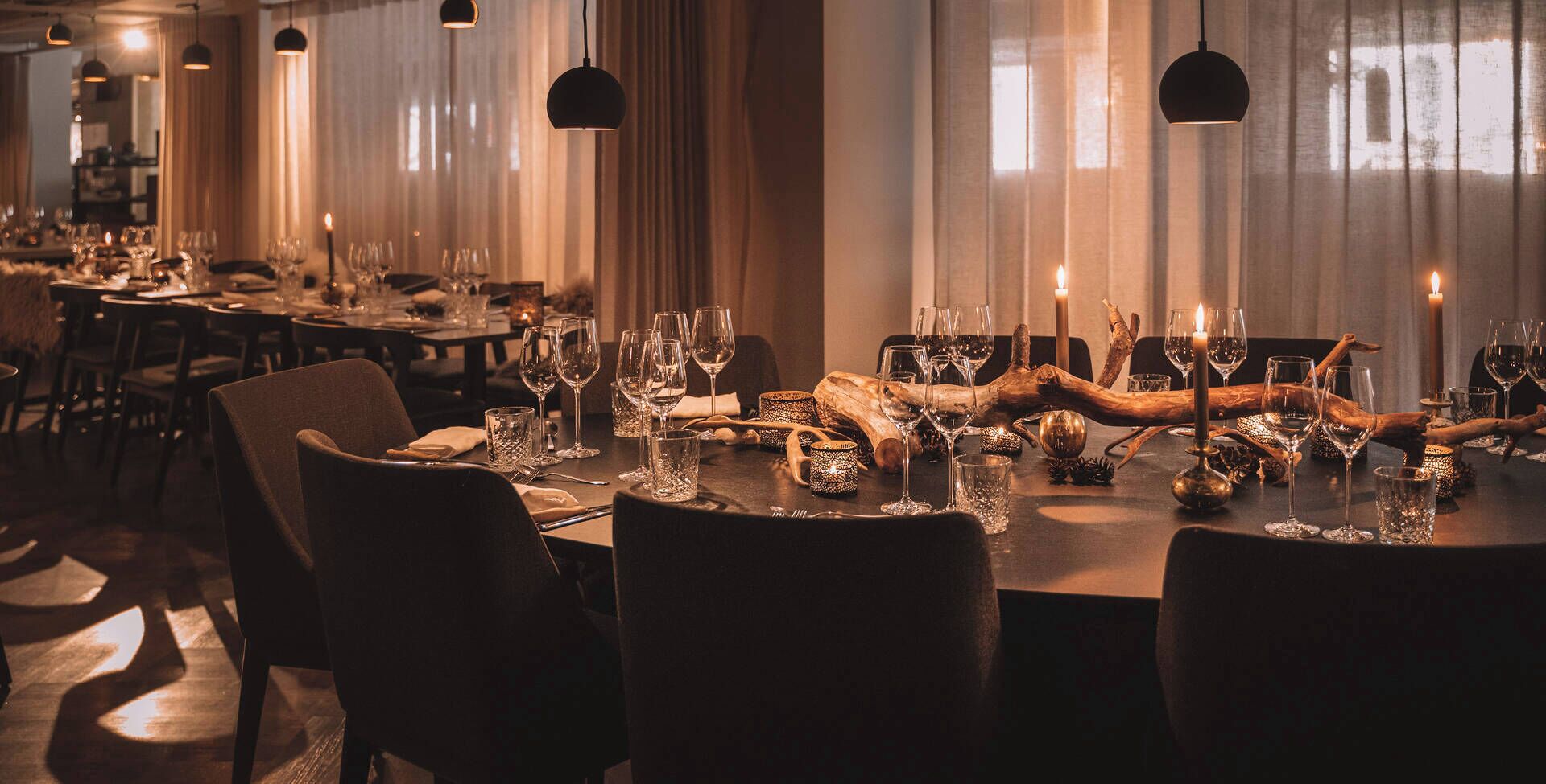 Un restaurante con varias mesas dispuestas para comer, con velas, copas de vino y elementos decorativos rústicos.