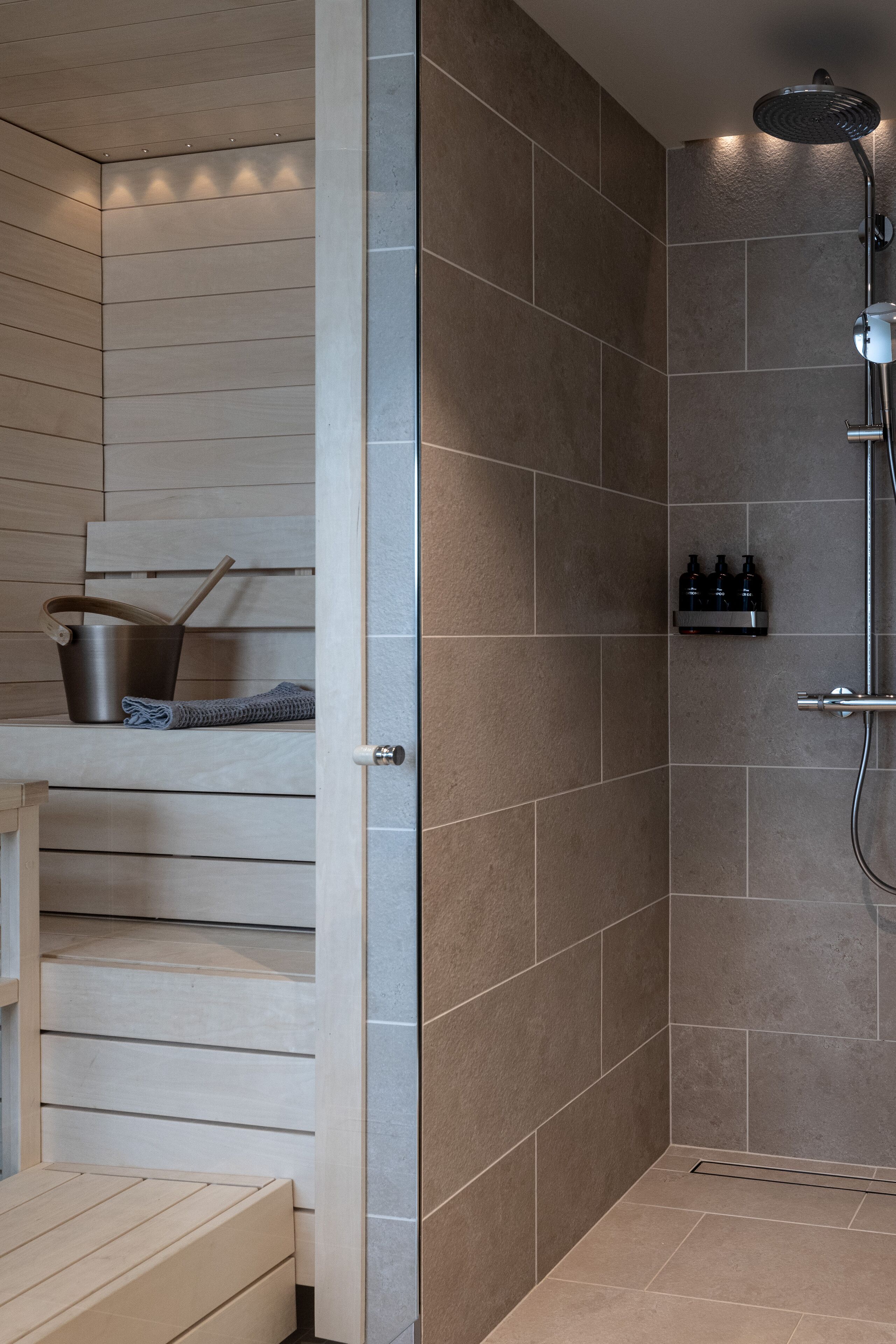 Un baño moderno con ducha, banco de madera y estante con artículos de aseo.