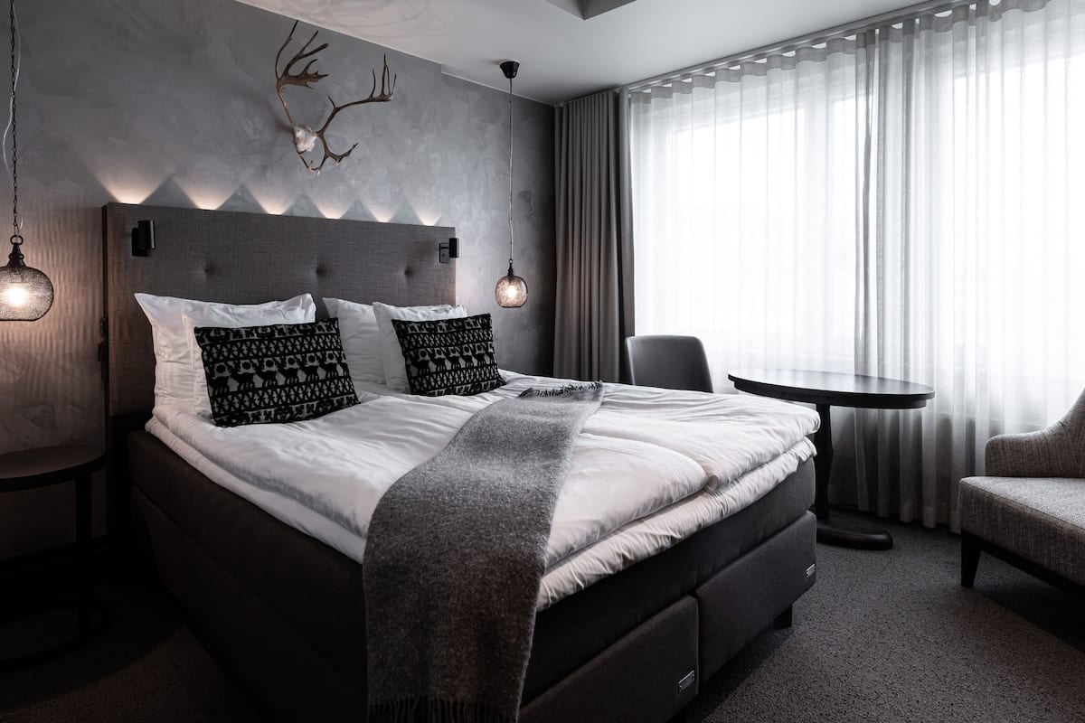 A modern bedroom with a large bed, bedside tables, a round table, and a chair.