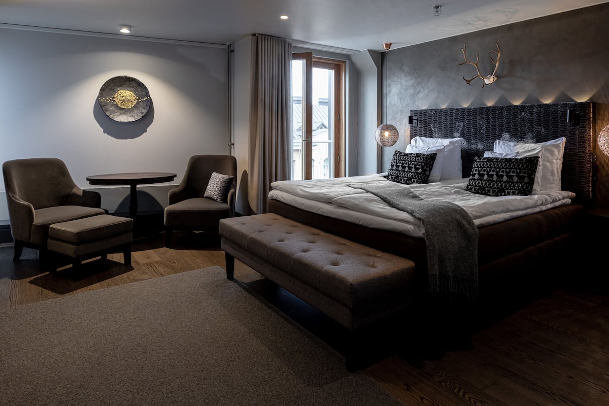 A modern bedroom with a large bed, two armchairs, a small table, and a bench.