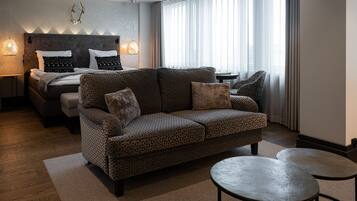 A modern hotel room with a patterned sofa, a bed with patterned pillows, a small table, and a decorative wall piece.